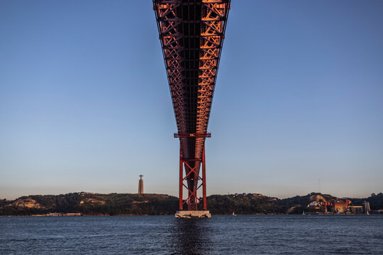 View of April 25th bridge crossing Tagus river in Lisbon downtown with Cristo Rei statue in background, Lisbon, Portugal.