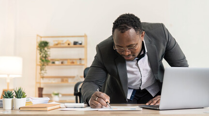 Obraz premium Professional male economist searches needed information on portable computer, happy to recieve high net profit, spends important banking operation. Black male trader analyzes financial market.