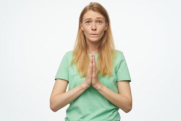 Indoor studio portrait of young ginger female with freckles press palms together and praying isolated over background