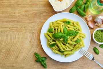 Penne pasta with pesto sauce on plate with wooden table background.Eesy and healthy vegetarian Italian food.Top view.Copy space