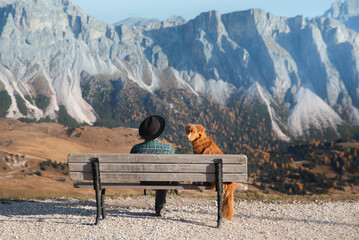 Naklejka na ściany i meble red dog and a boy sit on a bench and look at the mountains. Travel and adventure with your pet. Italy, Dolomites 