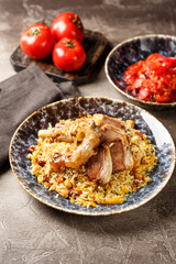 Pilaf with lamb meat in large dish and plate of tomato salad