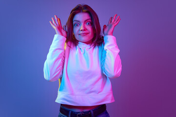 Plakat Emotional young girl with big eyes looking at camera with questioning face, posing against gradient blue purple studio background in neon light. Emotions, youth, lifestyle, facial expression concept