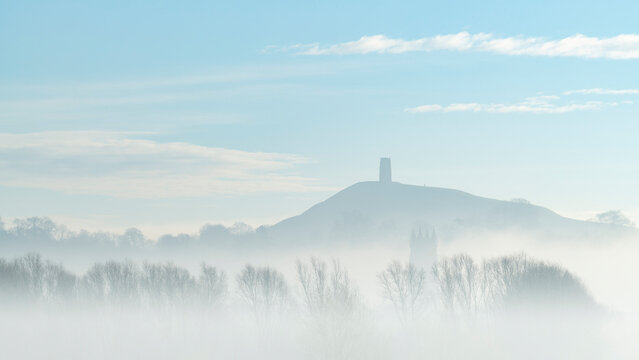 St. Michael's Tower on Glastonbury Tor above the tower of St. John the Baptist's Church on a misty morning in winter, Glastonbury, Somerset