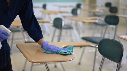 Teacher back at school after covid-19 quarantine and lockdown, disinfecting desks.