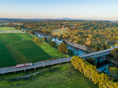 Red cattle truck on bridge travelling through green farmland in country