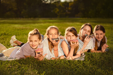 happy children girls eat sweet donuts in green park and have fun in summer camp. Friendship concept