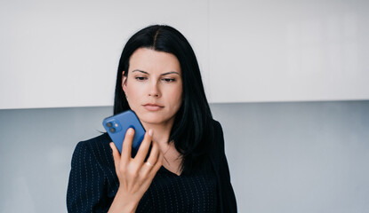 Shocked businesswoman in business suit holds phone looks at screen with unhappy face expression...