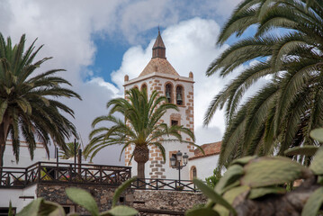 Fototapeta na wymiar Detalle del campanario de la iglesia blanca del pueblo de Betancuria, rodeado de muchas palmeras y algunos cactus en Fuerteventura Islas Canarias