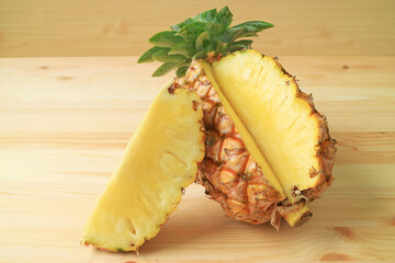 Piece of fresh ripe pineapple cut from the whole fruit isolated on wooden table