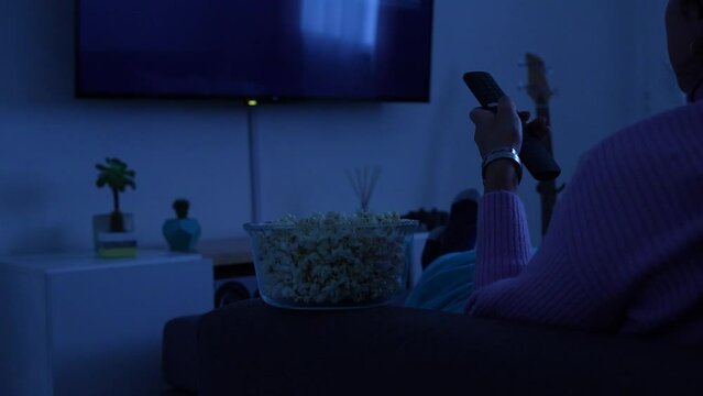 Woman watching Netflix on the sofa of her living room while eating popcorn. July 12, 2022. Rio Negro, Argentina
