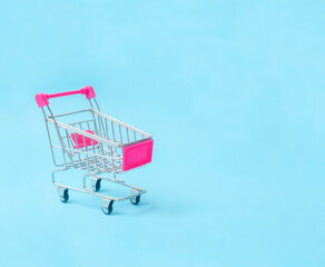 Close-up the empty toy metal supermarket shopping cart on blue  background with copy space.