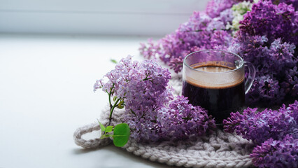 Obraz na płótnie Canvas glass cup of coffee on the windowsill. flowering branches of lilac. spring time