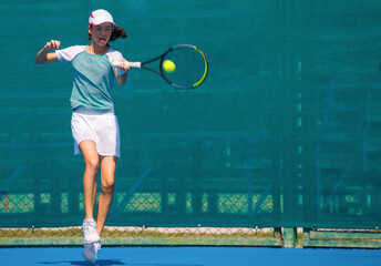 Fototapeta na wymiar A girl plays tennis on a court with a hard blue surface on a summer sunny day