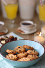 Plate of chocolate pralines, bowl of cookies, cups of tea, glasses of juice and lit candles on the table. Selective focus.