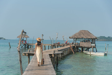 Woman traveler walk alone on wooden bridge into hidden bar on sea to relax on vacation in summer season