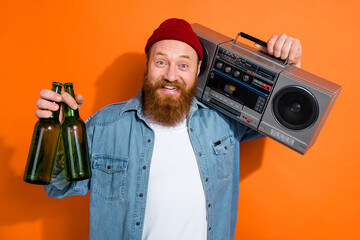 Photo of young virile excited optimistic guy listen vintage boombox hold two bottles alcohol beer party day isolated on orange color background