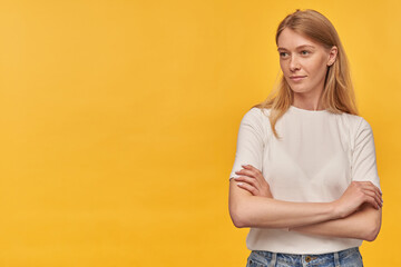 Obraz premium Indoor studio portrait of young ginger female with freckles looking into camera with serious facial expression, isolated over yellow orange background