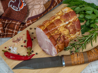 A piece of juicy and tasty bacon on a wooden cutting board with a carving knife, multi-colored allspice peas, red hot peppers, parsley, dill and basil. The concept of different meat preparation