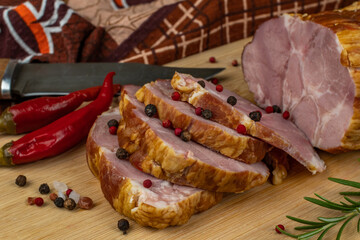 Slices of juicy and delicious pork bacon on a wooden cutting board with a carving knife, multi-colored allspice peas, red hot peppers, parsley, dill and basil. The concept of meat products