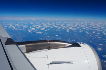 Naklejka na ściany i meble Aircraft engine and wing on the border of atmosphere and space. The edge of the troposphere. Horizon over the Earth. Flights, travel and tourism. View from a window or porthole. Clouds and blue sky.