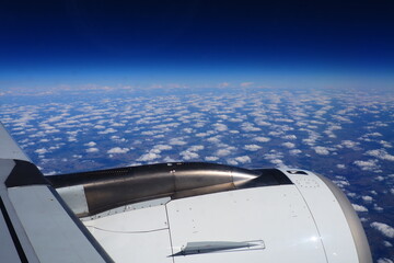 Aircraft engine and wing on the border of atmosphere and space. The edge of the troposphere. Horizon over the Earth. Flights, travel and tourism. View from a window or porthole. Clouds and blue sky.