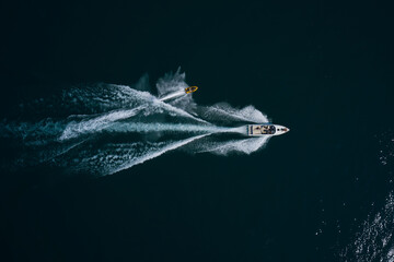 Speedboat and high speed water scooter movement on water. High speed white boat with people fast moving on dark water top view. Yellow water scooter movement on dark water. © Berg