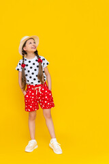 A little girl is looking at your ad. A beautiful child dressed in polka dot shorts and a hat is enjoying the summer looking at your advertisement on a yellow isolated background. Copy space.