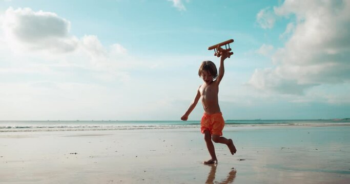 Happy boy run along the beach, lifting uo a toy plane and laughing