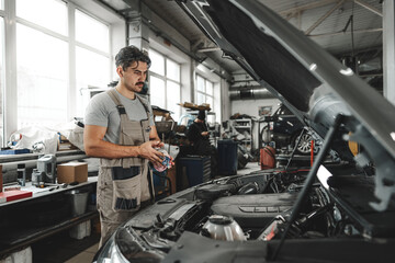 Young male mechanic examining engine under hood of car at the repair garage