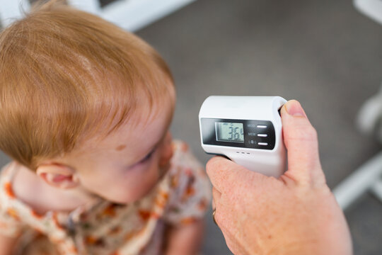Person pointing digital thermometer at baby head to check temperature