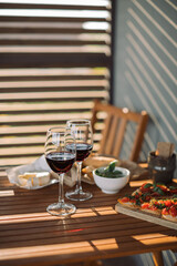 Red wine, cheese, olives, bruschetta with tomato and basil on summer terrace. Golden hour light. Copy space.