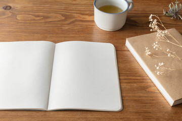 A brown wooden table with a white spread notebook, books, dried flowers and mugs in a natural style