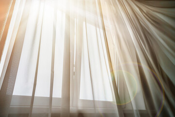 Bright sun rays lighting in house room through thin white curtain on warm summer day.