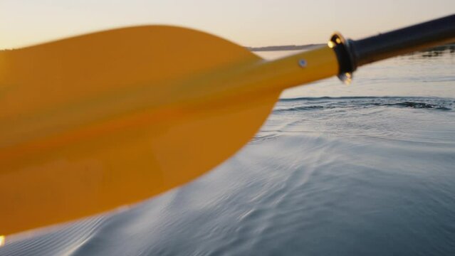 Traveler paddles on the smooth surface of the water at sunset in the golden hour, water travel, kayaking, rowing, active recreation