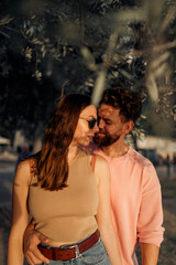 Young attractive cute couple in romantic honeymoon kissing and embracing each other at the sunset, bearded curly man and brunette girl in sunglasses 