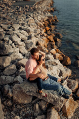 Young attractive cute couple in romantic honeymoon kissing and embracing each other at the sunset at Garda lake coast, bearded curly man and brunette girl in sunglasses 