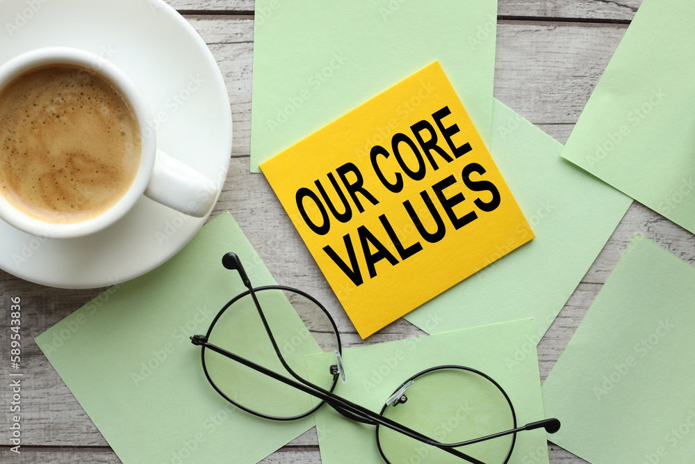 Poster colored note paper with text our core values symbol pinned to wood texture background and glasses
