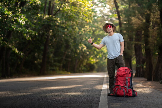 happy asian backpacker with bag hitchhiker for car passenger vehicle transportation for hobby adventure trekking travel trip outdoor nature forest in summer