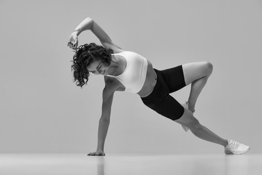 Black and white image. Young sportive woman in sportswear training, doing stretching exercises. Side plank position. Concept of sportive lifestyle, beauty, body care, fitness, health