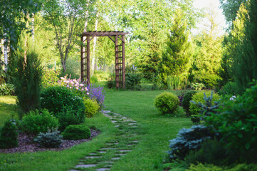 Beautiful summer garden view with curvy stone pathway and wooden archway. Natural woodland cottage...