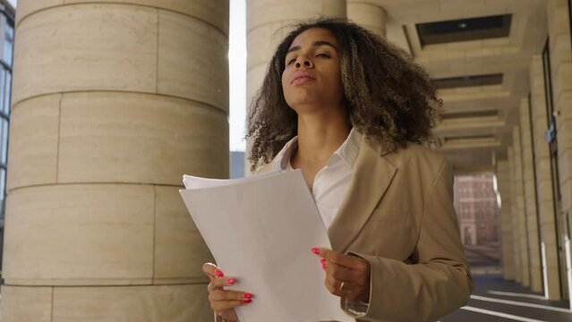Tired woman in business clothes throws up papers with documents walking down the street near a business center with columns. A new turn in life, tired of everything, fatigue, camera movement, slow