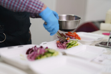 Cook preparing lunch boxes with sliced vegetables on a kitchen counter in a Greek restaurant.