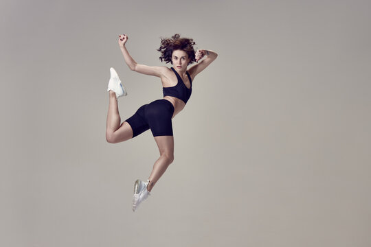High jump. Dynamic image of young beautiful woman in sportswear training, posing in motion against grey studio background. Concept of sportive lifestyle, beauty, body care, fitness, health