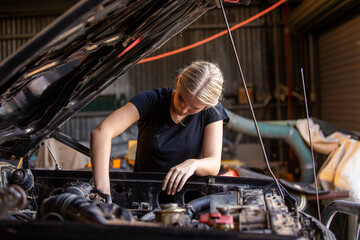 young female australian tradesperson mechanic working on car engine in auto repair garage