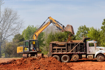 Dump truck is loading earth into an excavator on construction site