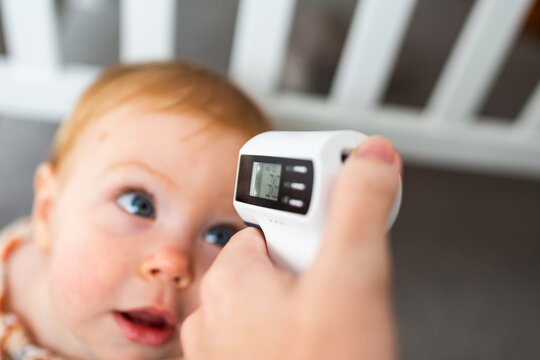 Person pointing digital thermometer at baby head to check temperature