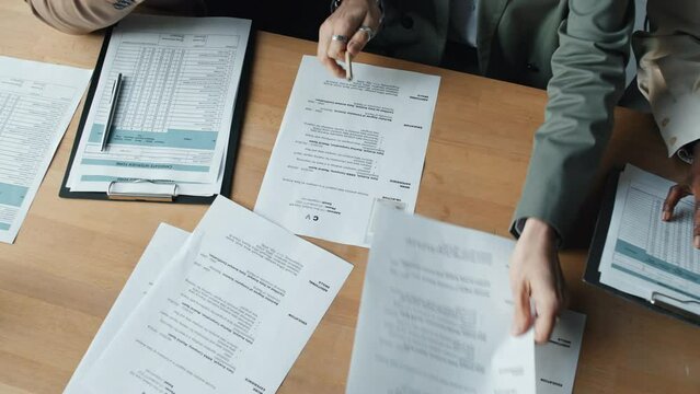 Close up of three HRs, Caucasian man and woman, as well as black woman, looking through CVs, making two all sitting at office table, seen from above