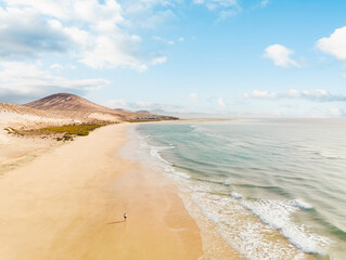 View from above, stunning aerial view of a person running on a beautiful beach bathed by the ocean and surrounded by beautiful sand dunes. Costa Calma, Fuerteventura, Canary Islands.