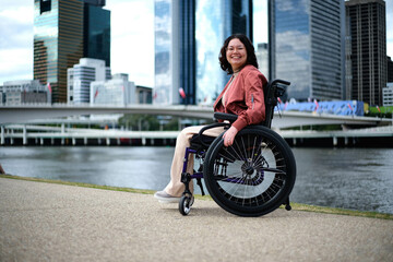 Happy woman in wheelchair in front of river with city in background